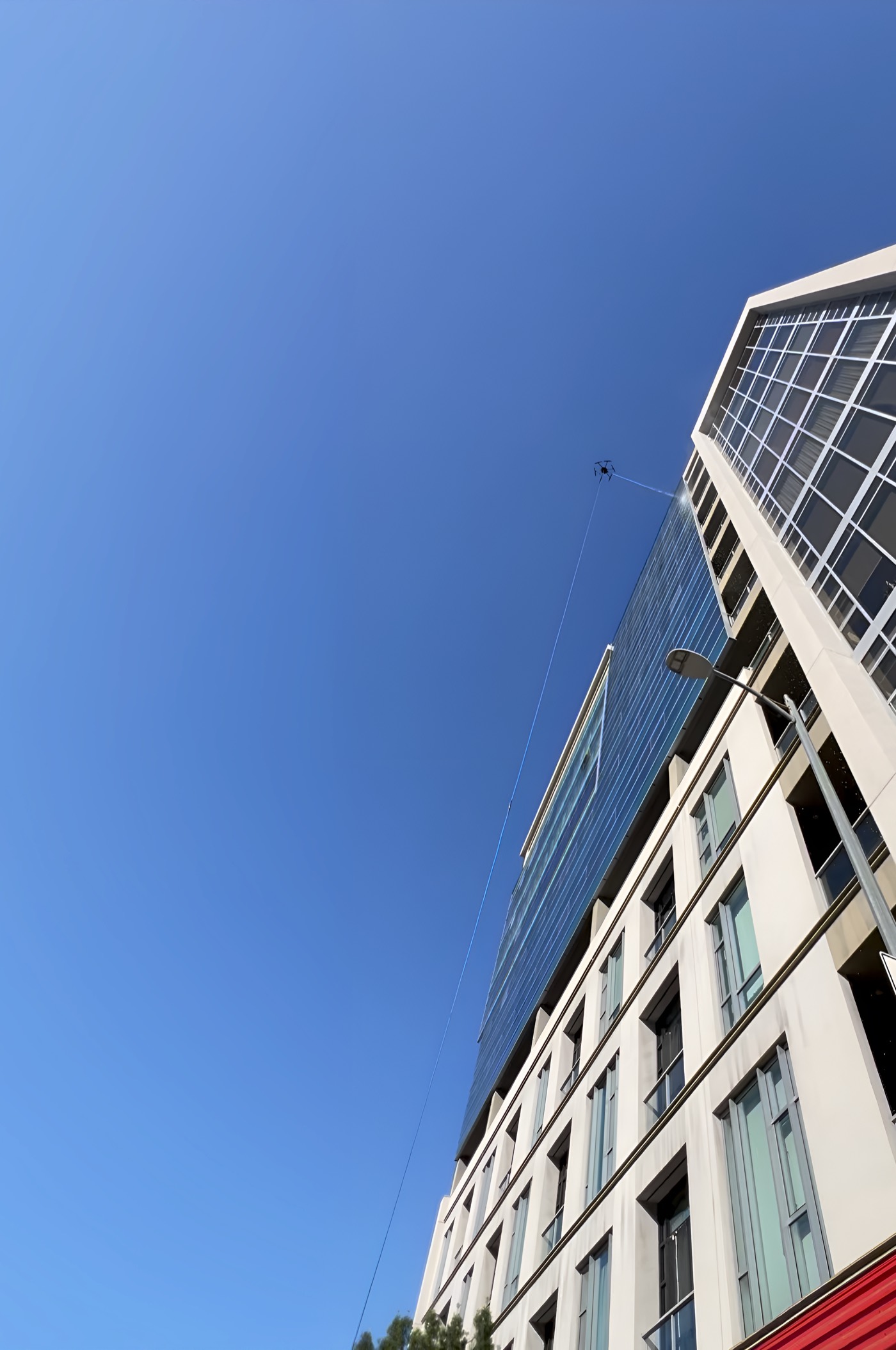 Looking up a high-rise as a Stratos drone cleans the upper glazing far above the street.
